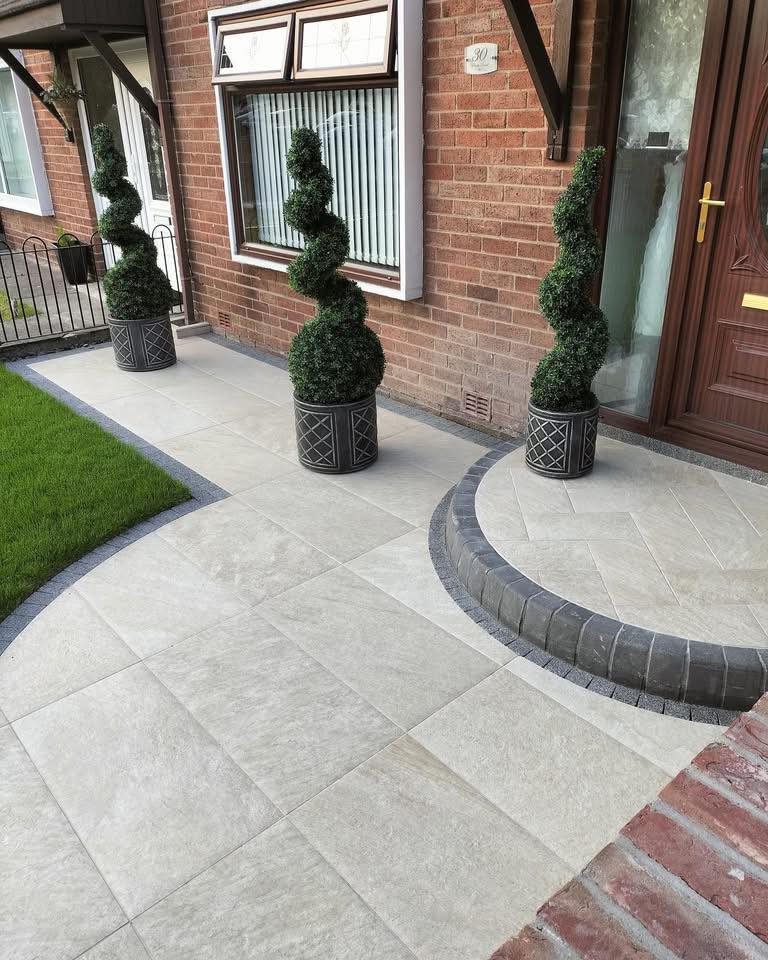 Curved front garden — light porcelain patio with dark block border and spiral topiary